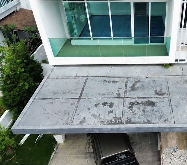 A bare concrete car porch slab with weathered, stained panels, a car parked beneath.