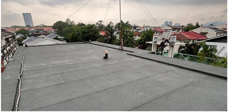 The flat roof finished in dark granular membrane, houses and trees behind.