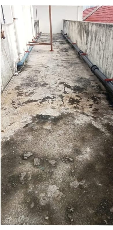A stained, worn upper-floor walkway between parapet walls, pipes along one side.