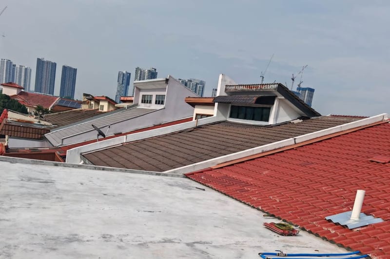 A finished dark membrane roof deck between red clay tiled roofs, Kuala Lumpur towers behind.