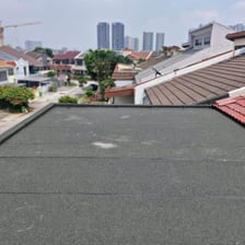 A finished dark membrane roof deck on a house, bounded by a low parapet, with neighbouring tiled roofs behind.